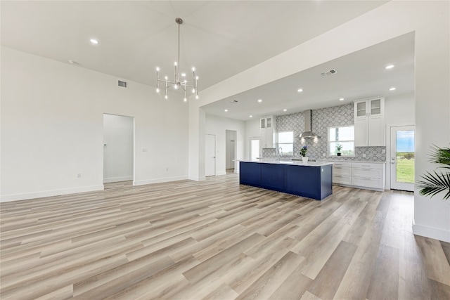 kitchen featuring decorative backsplash, wall chimney exhaust hood, decorative light fixtures, white cabinets, and a center island