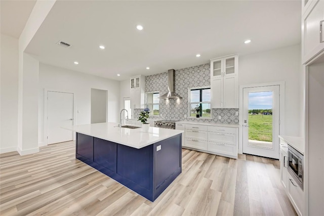 kitchen with white cabinetry, sink, wall chimney exhaust hood, a center island with sink, and appliances with stainless steel finishes