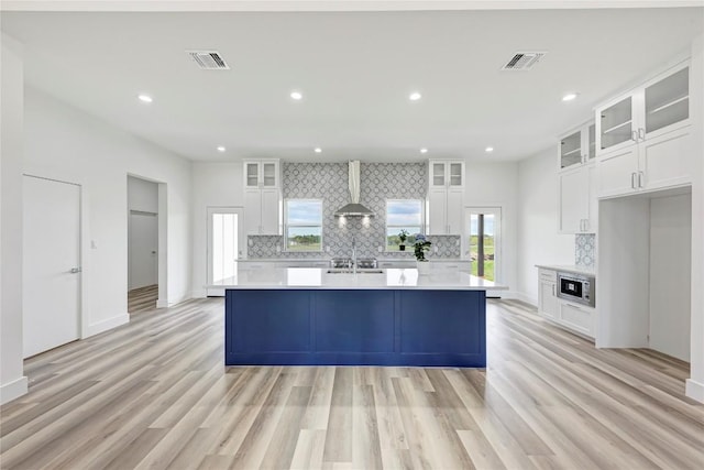 kitchen featuring wall chimney exhaust hood, decorative backsplash, a center island with sink, and white cabinets