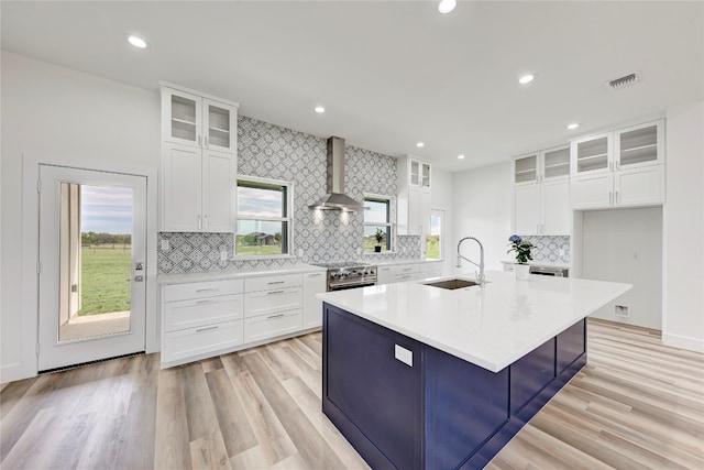 kitchen featuring a kitchen island with sink, wall chimney range hood, sink, high end stainless steel range, and white cabinetry