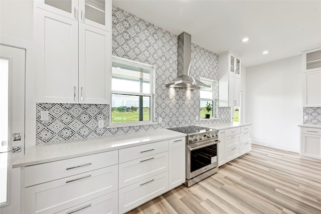 kitchen with white cabinets, wall chimney range hood, high end stainless steel range, light wood-type flooring, and light stone counters