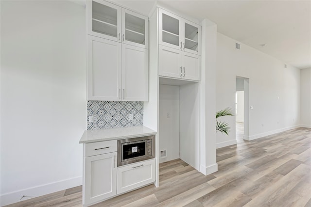 kitchen with white cabinets, stainless steel microwave, light wood-type flooring, and backsplash