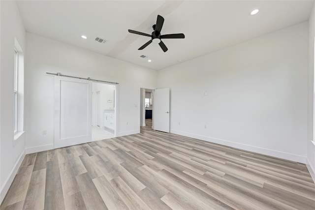 unfurnished bedroom with ceiling fan, a barn door, light hardwood / wood-style flooring, multiple windows, and connected bathroom