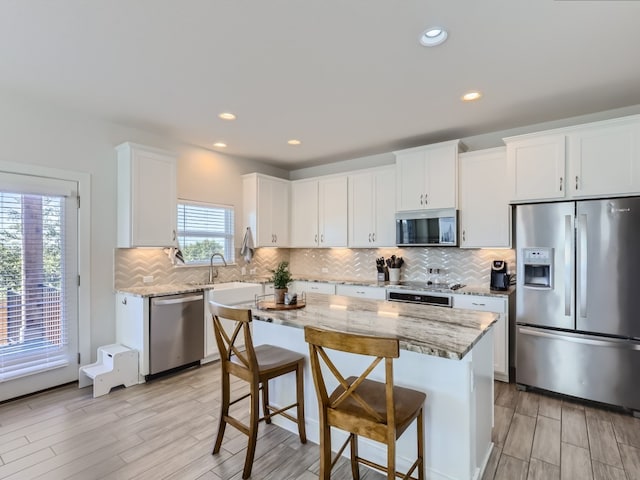 kitchen featuring a breakfast bar, light stone counters, tasteful backsplash, white cabinetry, and stainless steel appliances