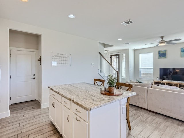 kitchen featuring white cabinetry, ceiling fan, light wood-type flooring, a center island, and a breakfast bar area