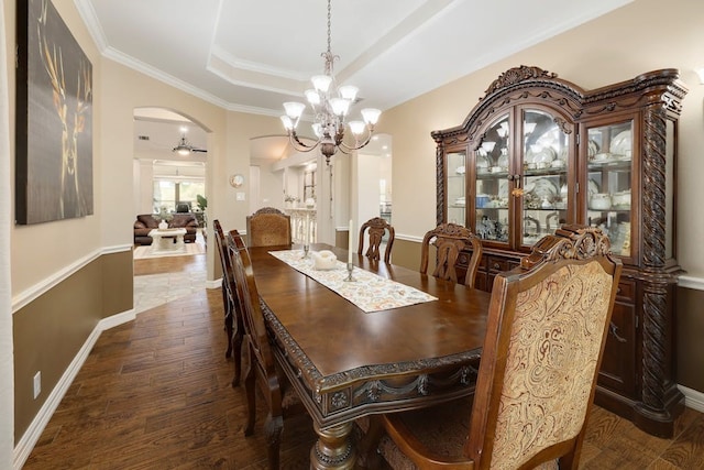 dining room with dark wood-type flooring, a tray ceiling, and ceiling fan with notable chandelier