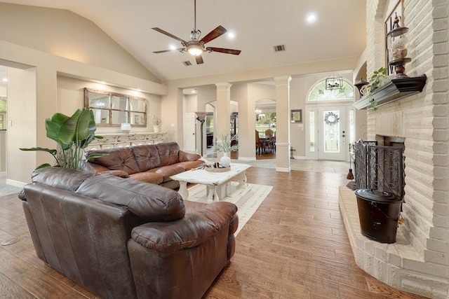 living room featuring ceiling fan, decorative columns, a fireplace, high vaulted ceiling, and light hardwood / wood-style flooring