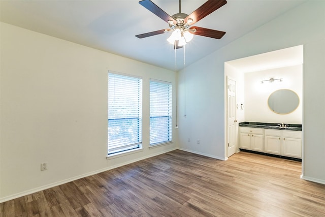 empty room featuring ceiling fan, vaulted ceiling, sink, and light hardwood / wood-style floors