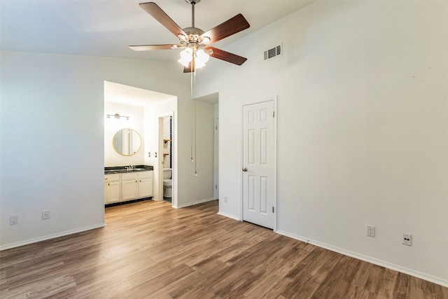 unfurnished bedroom with connected bathroom, hardwood / wood-style floors, ceiling fan, and high vaulted ceiling