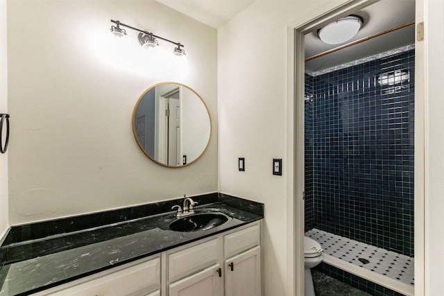 bathroom with toilet, a tile shower, and vanity with extensive cabinet space