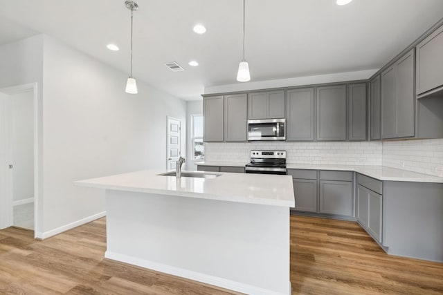 kitchen with gray cabinetry, sink, stainless steel appliances, and a kitchen island with sink