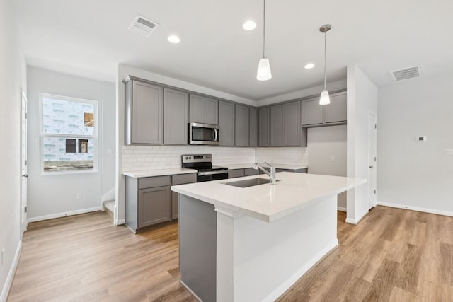 kitchen featuring gray cabinetry, sink, stainless steel appliances, light hardwood / wood-style flooring, and an island with sink