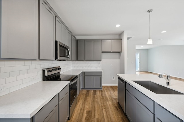 kitchen with appliances with stainless steel finishes, gray cabinetry, sink, hardwood / wood-style flooring, and hanging light fixtures