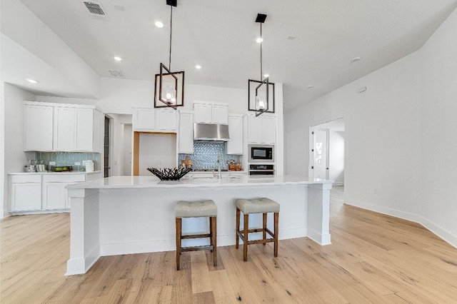 kitchen featuring white cabinetry, decorative light fixtures, black microwave, and a spacious island