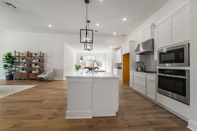 kitchen with a kitchen island with sink, white cabinetry, black microwave, decorative light fixtures, and stainless steel oven