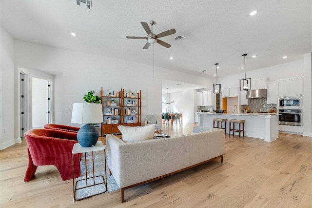 living room with ceiling fan, a textured ceiling, and light wood-type flooring