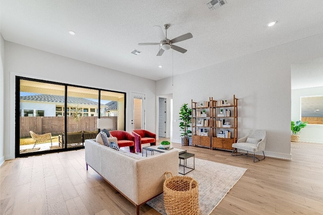 living room with a textured ceiling, ceiling fan, and light hardwood / wood-style flooring