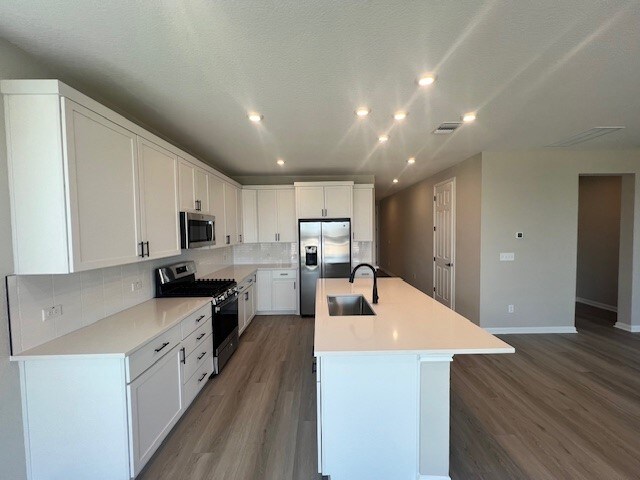 kitchen with a center island with sink, sink, appliances with stainless steel finishes, and hardwood / wood-style flooring