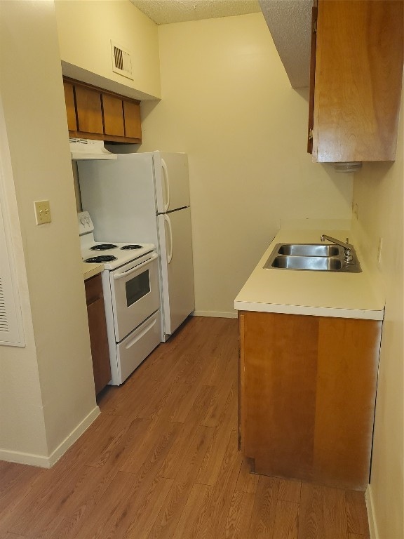 kitchen with a textured ceiling, white appliances, light hardwood / wood-style flooring, and sink