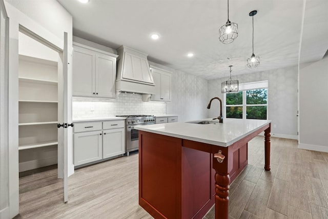 kitchen with decorative light fixtures, a center island with sink, stainless steel stove, custom exhaust hood, and sink