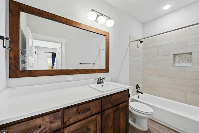 full bathroom with wood-type flooring, tiled shower / bath, vanity with extensive cabinet space, and toilet