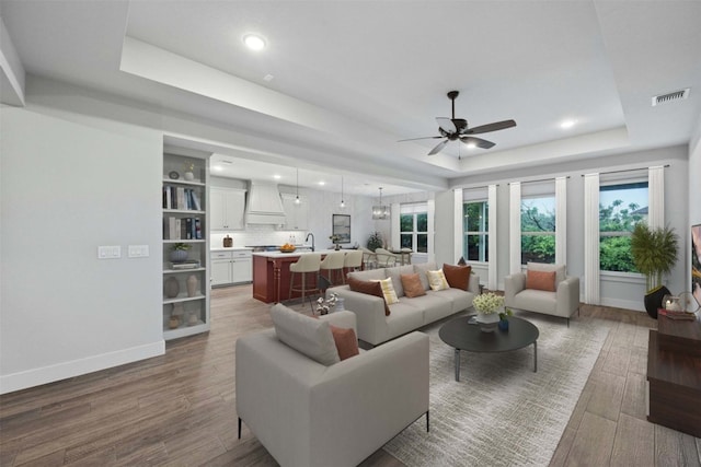 living room featuring sink, ceiling fan, a tray ceiling, and hardwood / wood-style flooring