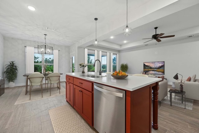 kitchen with sink, dishwasher, a raised ceiling, decorative light fixtures, and a kitchen island with sink