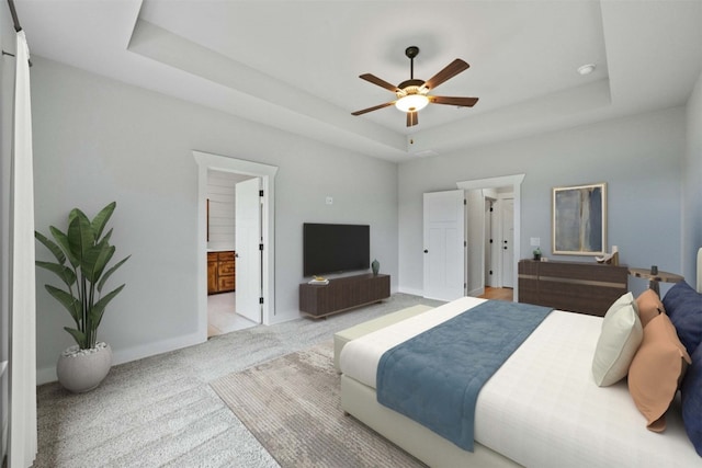 bedroom featuring light carpet, ceiling fan, ensuite bath, and a tray ceiling