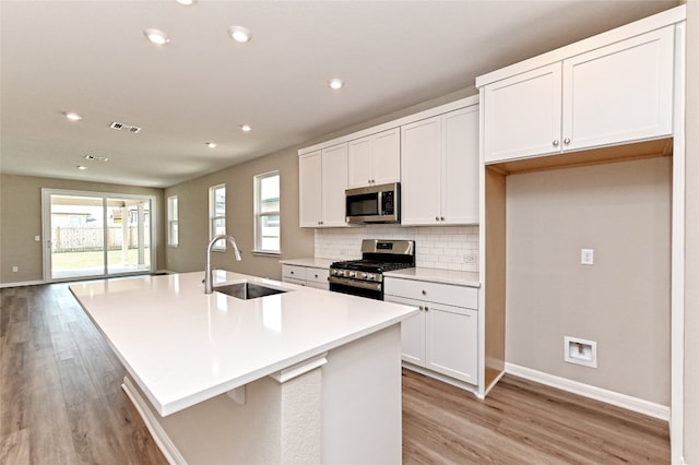 kitchen featuring sink, a kitchen island with sink, white cabinetry, stainless steel appliances, and light wood-type flooring