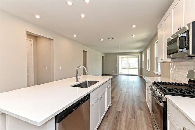 kitchen with sink, an island with sink, light hardwood / wood-style flooring, backsplash, and appliances with stainless steel finishes