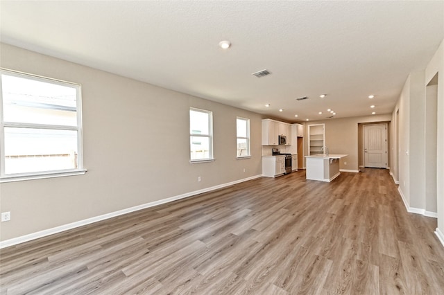 unfurnished living room featuring sink, light hardwood / wood-style floors, and a textured ceiling