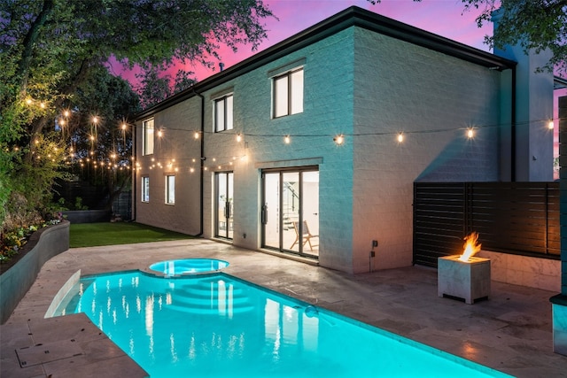 back house at dusk with a swimming pool with hot tub, a patio area, and french doors