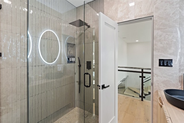 bathroom featuring wood-type flooring, vanity, a shower with door, and tile walls