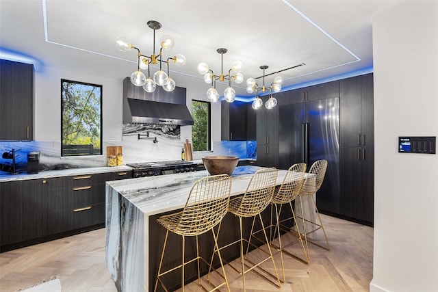 kitchen with a center island, wall chimney exhaust hood, hanging light fixtures, a kitchen breakfast bar, and decorative backsplash