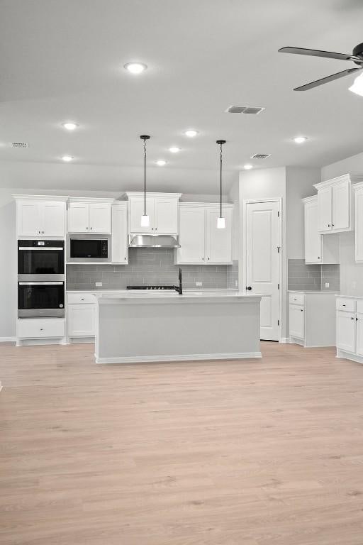 kitchen featuring decorative light fixtures, stainless steel microwave, multiple ovens, and white cabinets