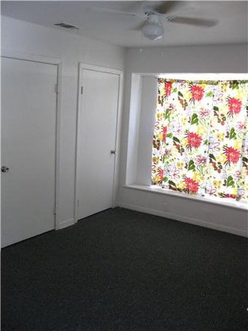 unfurnished room featuring ceiling fan and dark colored carpet