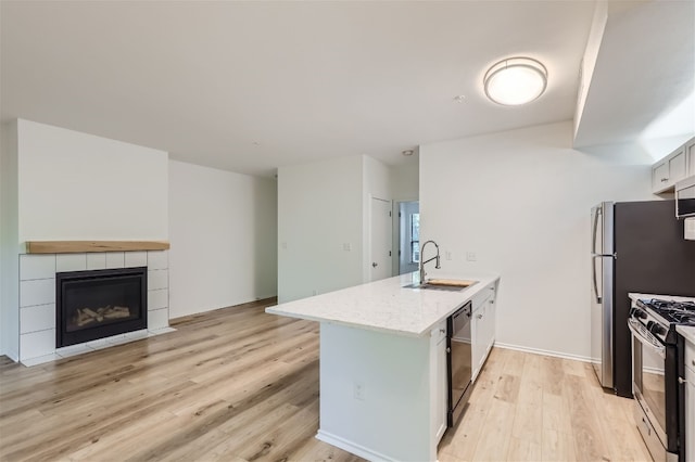 kitchen with kitchen peninsula, light wood-type flooring, white cabinets, stainless steel gas stove, and a tiled fireplace