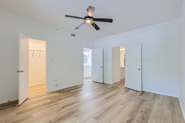 unfurnished bedroom with ensuite bath, light hardwood / wood-style flooring, ceiling fan, a spacious closet, and a closet