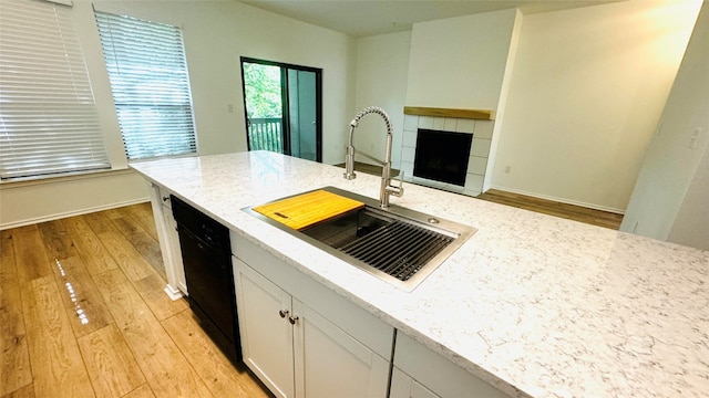 kitchen with light stone countertops, sink, light hardwood / wood-style flooring, dishwasher, and a tiled fireplace