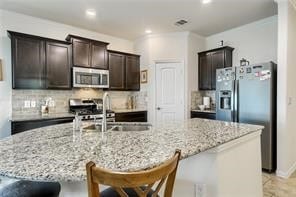 kitchen featuring light stone countertops, a kitchen bar, dark brown cabinetry, and stainless steel appliances