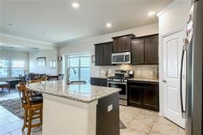 kitchen with light stone counters, an island with sink, a breakfast bar area, stainless steel appliances, and light tile floors