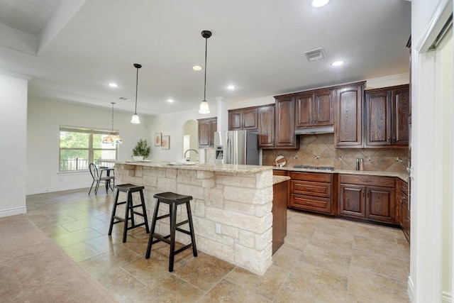 kitchen featuring appliances with stainless steel finishes, tasteful backsplash, decorative light fixtures, a center island with sink, and a breakfast bar area