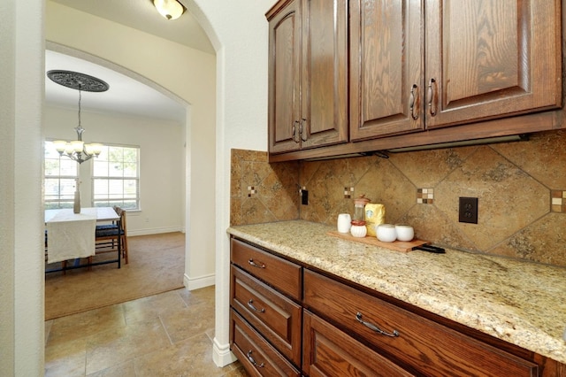 kitchen with decorative backsplash, light stone counters, and an inviting chandelier