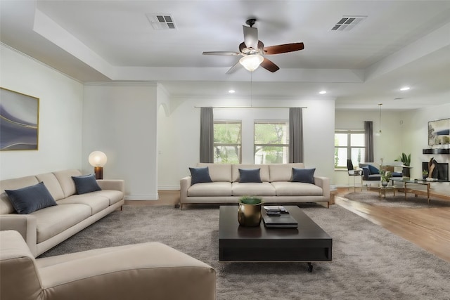 living room featuring hardwood / wood-style floors, ceiling fan, and a raised ceiling