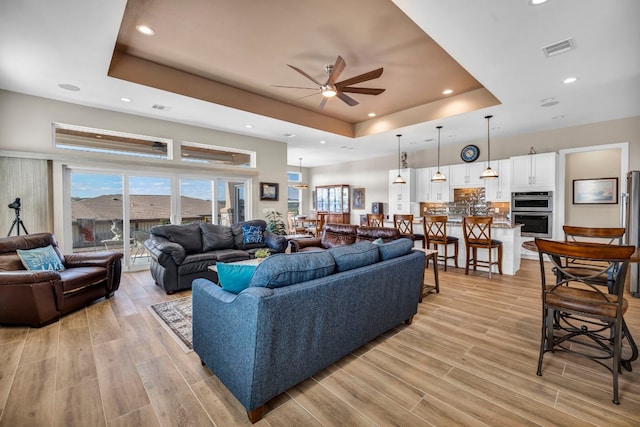 living room with light hardwood / wood-style floors, ceiling fan, and a raised ceiling