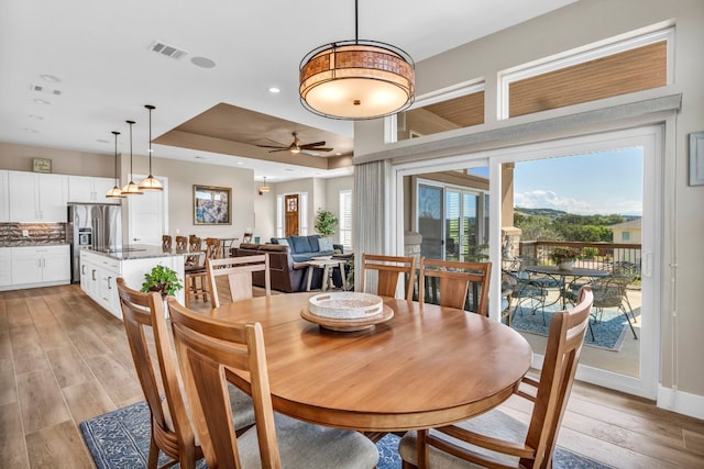 dining room with a tray ceiling, ceiling fan, and light hardwood / wood-style floors