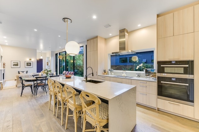 kitchen featuring a center island with sink, decorative light fixtures, range hood, a breakfast bar, and sink