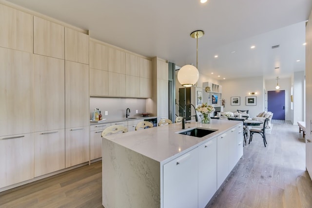 kitchen with sink, pendant lighting, hardwood / wood-style flooring, and an island with sink