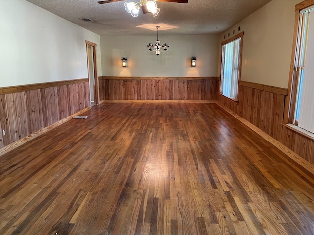 empty room featuring ceiling fan with notable chandelier, a textured ceiling, and dark hardwood / wood-style flooring