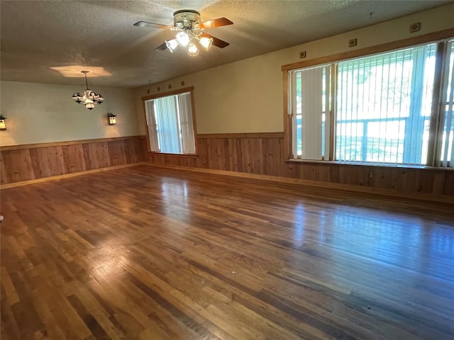 unfurnished room featuring ceiling fan with notable chandelier, a textured ceiling, and dark wood-type flooring